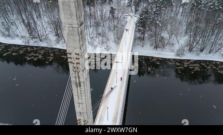 Drohnenfotografie von Betonsteg bedeckt von Schnee und Fußgängern, die während des bewölkten Wintertages überqueren Stockfoto