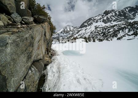 Pacific Crest Trail. Eine Bergkette mit einem großen Wasserkörper im Vordergrund. Das Wasser ist gefroren und der Schnee stapelt sich auf den Felsen. Die sce Stockfoto