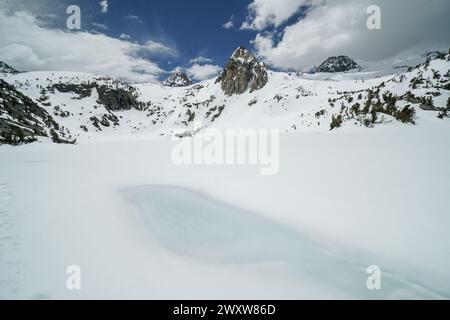 Pacific Crest Trail. Ein großer Wasserkörper ist in einer verschneiten Landschaft gefroren. Der Himmel ist klar und blau, mit ein paar Wolken verstreut. Die Stockfoto