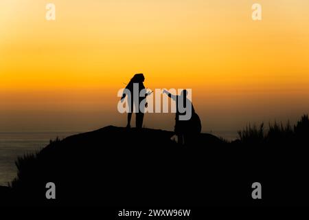 Silhouette einer Gruppe von Freunden, die im Sommer den Sonnenuntergang auf einer Klippe in der Nähe des Meeres genießen Stockfoto