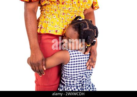 Ein wütendes Mädchen, das in Uniform auf weißem Hintergrund steht und Angst hat, zur Schule zu gehen und sich an ihre Mutter zu Klammern. Stockfoto