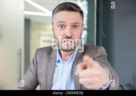 Ein wütender Geschäftsmann, der mit dem Finger zeigt, während er wütend über einen Videoanruf spricht und Frustration und Aggressivität zeigt. Stockfoto