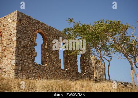 Ruinen eines überdachlosen Steingebäudes mit drei großen Fenstern stehen neben einer Baumgruppe auf der Burg Myrina auf der Insel Lemnos, Griechenland Stockfoto