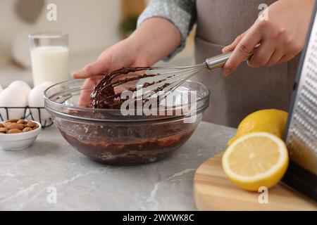 Frau mischt Schokoladencreme mit Schneebesen in einer Schüssel an einem grauen Marmortisch drinnen, Nahaufnahme Stockfoto