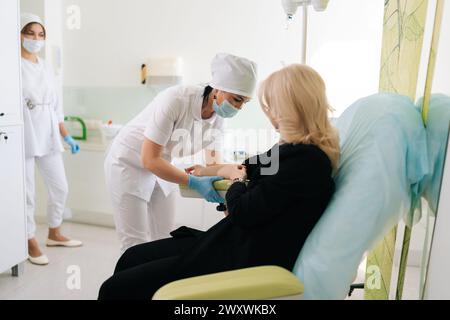 Seitenansicht Krankenschwester in medizinischer Uniform mit Wollvene abwischen, wo Nadel mit IV-Katheter eingeführt wird. Der Arzt führt die IV-Nadel in den Arm des Patienten ein Stockfoto