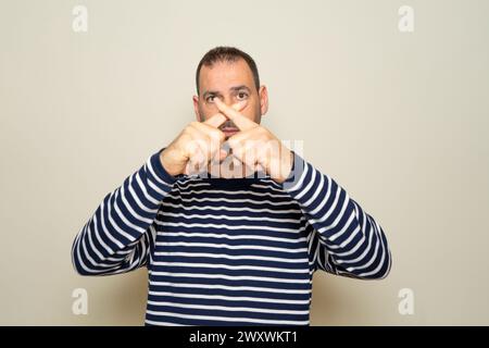 Hispanischer Mann mit Bart in seinen 40ern, der einen gestreiften Pullover über isoliertem beigefarbenem Hintergrund trug Stockfoto