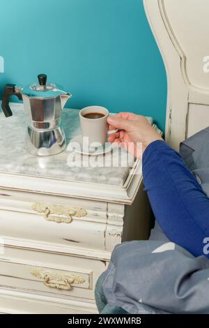 Frau, die im Bett liegt und beim Aufwachen mit einer Tasse Kaffee frühstückt Stockfoto