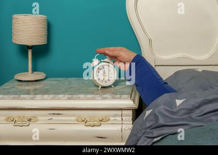 Die Frau im Bett legt den Arm aus, um morgens den Wecker auszuschalten Stockfoto