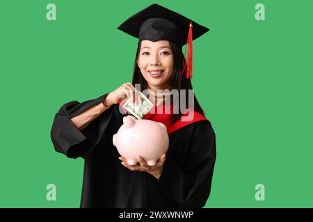 Asiatische Studentin, die Geld in Sparschweine auf grünem Hintergrund investiert. Studiengebühren-Konzept Stockfoto