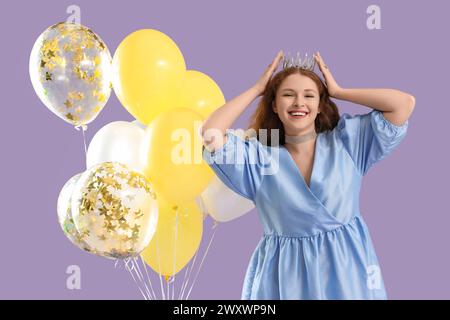 Junge Rothaarige Frau in Krone mit Ballons auf Fliederhintergrund Stockfoto