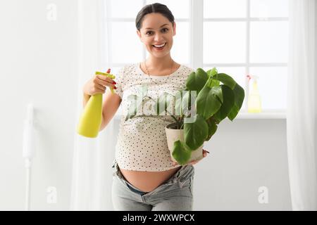 Junge schwangere Frau, die eine Zimmerpflanze in einer neuen Wohnung tränkt Stockfoto