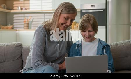 Kaukasische ältere Frau 50er mit Enkel, die in den sozialen Medien auf Laptop-Shopping im Online-Shop spricht lächelnd lachend zu Hause Couch-Pflege Stockfoto
