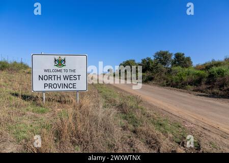 Landschaft einer Schotterstraße mit einem Straßenschild mit der Aufschrift Willkommen in der Nordwestprovinz bei Stilfontein. Stockfoto