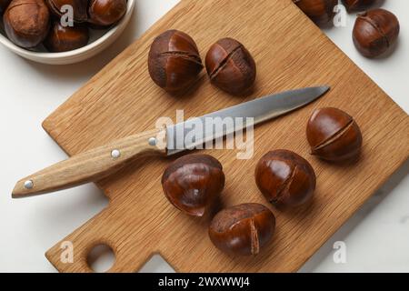 Geröstete, essbare Kastanien und Messer auf weißem Tisch, flache Ladefläche Stockfoto