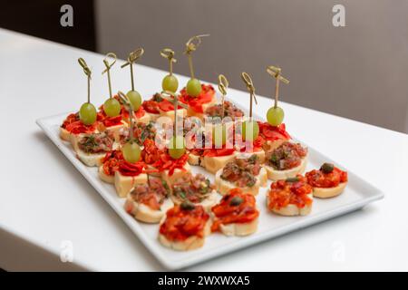 Teller mit verschiedenen Meeresfrüchten und Fleischkanapees. Canape auf weißem Keramiktablett, pastös, Bäckerei, frisch. Catering-Konzept. Stockfoto