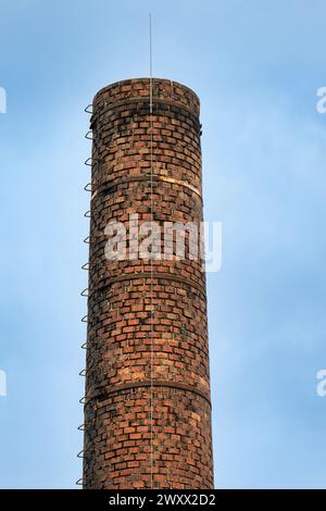 Historischer Fabrikschornstein aus Mauerwerk mit Steigeisen und modernem Blitzleiter Stockfoto