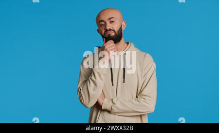 Eine Person aus dem Nahen Osten, die über eine Sache vor der Kamera nachdenkt, nachdenklich und verwirrt handelt, während sie versucht, eine Entscheidung zu treffen. Ein arabischer Typ, der sich nachdenklich und unsicher über eine Frage benimmt. Kamera 1. Stockfoto