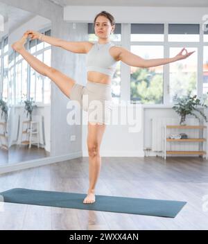 Erfahrenes junges Mädchen in Activewear, das Yoga-Vogel des Paradieses, Svarga Dvijasana im Fitnessstudio macht Stockfoto