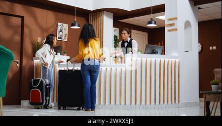 Asiatische Touristen betreten die Hotellobby und nutzen die Serviceklingel, rufen die Mitarbeiter an und bieten Unterstützung beim Check-in an. Reisende, die Hilfe von der Rezeption und dem Hotelgewerbe anfordern. Stockfoto