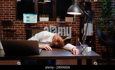 Müder Angestellter, der auf dem Schreibtisch geschlafen hatte, nachdem er die ganze Nacht mit dem Schreiben von E-Mails zu kämpfen hatte. Schläfrige Geschäftsfrau, die im Büro schläft, nachdem sie über Nacht gearbeitet hat, im Laptop geschlafen hat, Kamera A Stockfoto