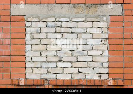 Alter alter verwitterter roter Backsteinmauerhintergrund, gemauerte Schuppen-Fensteröffnung, gemauerte weiße beschädigte Kalziumsilikat-Sand-Kalksteine, grungy Stockfoto