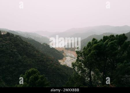 Marbella Istan Reservoir, Eine ruhige Szene eines sich windenden Flusses, der durch ein üppiges Tal fließt, mit Nebel bedeckt die fernen Hügel und einem einsamen Ort Stockfoto