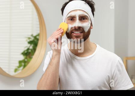 Mann mit Stirnband, der sein Gesicht mit Schwamm im Badezimmer wäscht Stockfoto