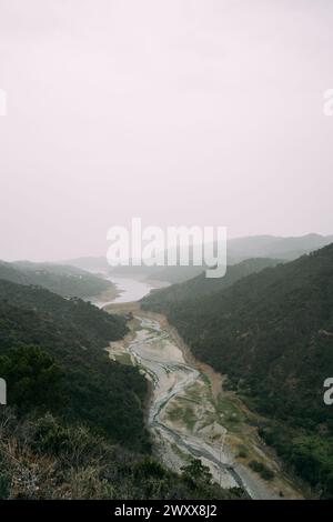 Marbella Istan Reservoir, Eine ruhige Szene eines sich windenden Flusses, der durch ein üppiges Tal fließt, mit Nebel bedeckt die fernen Hügel und einem einsamen Ort Stockfoto