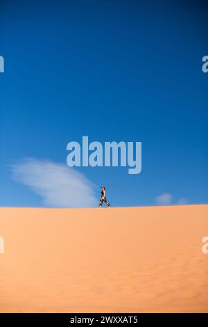 Frau, die auf einer Sanddüne in der Wüste im Coral Pink Sand Dunes State Park, Utah, spaziert Stockfoto