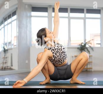 Eine aktive junge Lehrerin spielt Girlanden-Pose im Yoga-Studio Stockfoto