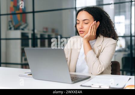 Verschlafene, müde brasilianische oder hispanische Geschäftsfrau mit lockigen Haaren, Finanzmanagerin des Unternehmens, sitzt mit geschlossenen Augen in einem modernen Büro, schlief während der Arbeitszeit ein Stockfoto