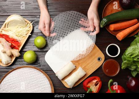 Köstliche Frühlingsbrötchen machen. Frau mit frischem Reispapier am Holztisch, flacher Lay Stockfoto