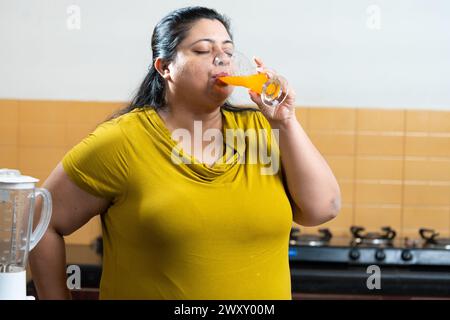 Übergewichtige fette indische Frau, die einen Fruchtsaft in einer Küche trinkt.Healthy Eating Konzept. Stockfoto