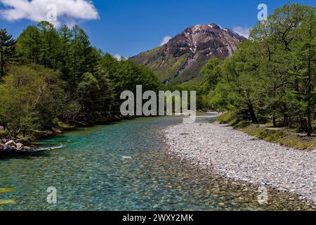 Klarer, schnell fließender Fluss, der durch einen Wald zu hoch aufragenden Berggipfeln führt (Hotaka, Matsumoto, Nagano) Stockfoto