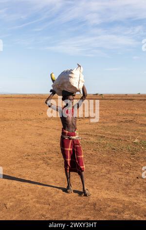 Omorate, Omo Valley, Äthiopien - 11. Mai 2019: Ein Mann aus dem afrikanischen Stamm Dasanesh trägt eine Tasche auf dem Kopf. Daasanach sind die Bewohner der kushitischen ethnischen Gruppe Stockfoto