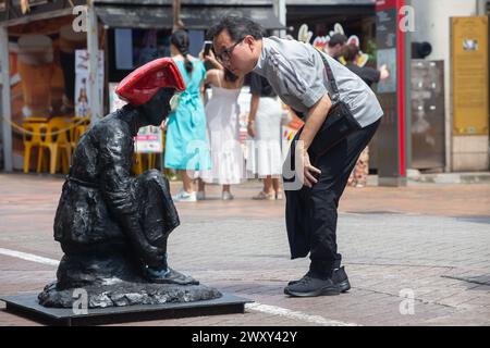 3. April 2024. Ein Mann in den 50ern, senkte seinen Oberkörper, um die Samsui Frau Statue im Detail zu studieren, Chinatown Street. Singapur. Stockfoto