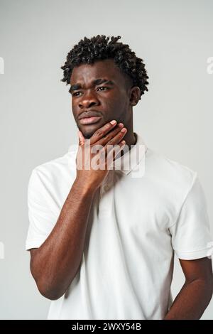 Junger Mann mit Pensive Expression, der sein Kinn vor grauem Hintergrund berührt Stockfoto