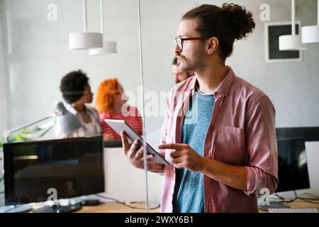 Glücklicher junger Hipster-Geschäftsmann, der ein digitales Tablet hält und im Startup-Büro arbeitet Stockfoto