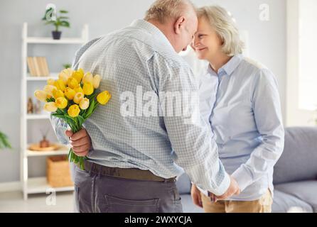 Ein älterer Mann mit Tulpen, der seiner lächelnden Frau zum Hochzeitstag ein romantisches Geschenk macht. Stockfoto