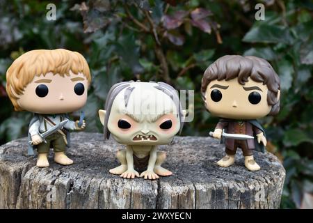 Funko Pop Actionfiguren von Sam, Gollum und Frodo aus dem Fantasy-Film der Herr der Ringe. Dunkler Wald, Baumstumpf, grüne Blätter. Stockfoto