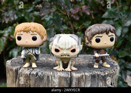 Funko Pop Actionfiguren von Sam, Gollum und Frodo aus dem Fantasy-Film der Herr der Ringe. Dunkler Wald, Baumstumpf, grüne Blätter. Stockfoto