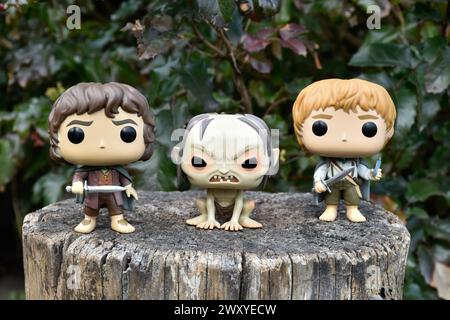 Funko Pop Actionfiguren von Frodo, Gollum und Sam aus dem Fantasy-Film der Herr der Ringe. Dunkler Wald, Baumstumpf, grüne Blätter. Stockfoto