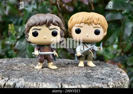 Funko Pop Actionfiguren der Hobbits Frodo und Sam aus dem Fantasy-Film der Herr der Ringe. Dunkler Wald, Baumstumpf, grüne Blätter. Stockfoto