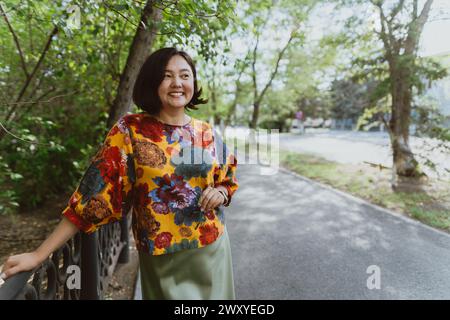 Stilvolle Dame mit einem trendigen, floralen Oberteil steht neben dem Parkgeländer Stockfoto