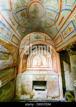 Die gewaltige Krypta unter dem Hauptaltar, die von Luigi Carimini 1869-71 erbaut wurde und neben den Überresten der Titularapostel Philipp und Jakobus auch die Reliquien verschiedener anderer Märtyrer, die bei diesen Ausgrabungen ans Licht kamen, vereint. und die Gräber von zwei Riario, die einst das Recht hatten, im Presbyterium zu begraben. Die Tempera-Dekoration des Ambulatoriums ist von den Katakomben von San Callisto und Domitilla inspiriert. - Basilica dei Santi XII Apostoli - Rom Italien Stockfoto