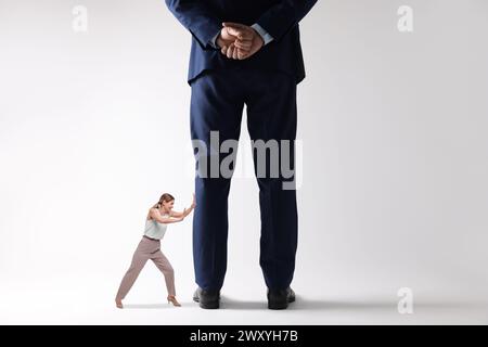 Eine kleine Frau schiebt einen riesigen Mann auf hellen Hintergrund Stockfoto