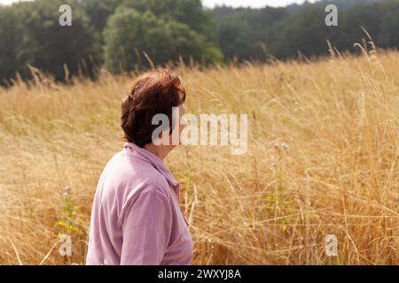 Reife Frau, die mitten auf einem Feld mit hohem Gras steht Stockfoto