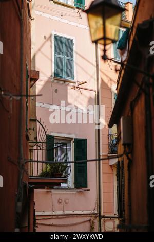 Ein bezaubernder Blick auf ein pinkfarbenes Fassadengebäude mit grünen Fensterläden, eingebettet in eine gemütliche Gasse mit einer alten Straßenlampe Stockfoto