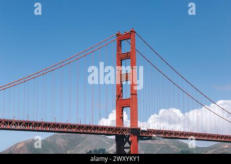 Die legendäre Golden Gate Bridge steht hoch unter dem hellblauen Frühlingshimmel, ergänzt durch flauschige weiße Wolken und sanfte Hügel Stockfoto