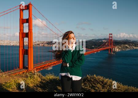 Eine junge Frau genießt die Wärme der Frühlingssonne mit der berühmten Golden Gate Bridge und der Skyline von San Francisco in der Ferne Stockfoto